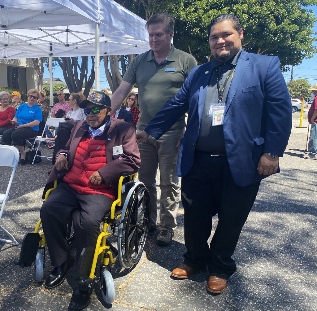 Disabled veteran Roger Santos sits in his new wheelchair as Bob Harris, Executive Director of the Gold Coast Veterans Foundation and Miguel Rodriguez, Community Outreach Manager of the Port of Hueneme look on.