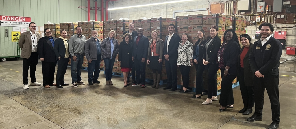 A group of people stands in a warehouse in front of stacked boxes, posing for a group photo.