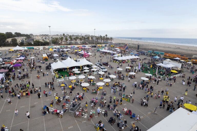 A large outdoor event with tents, food trucks, and crowds of people in a parking lot near the beach and pier celebrates the $3.935 Million State Grant for Port of Hueneme as Governor ramps up the California Port Data Partnership Program.
