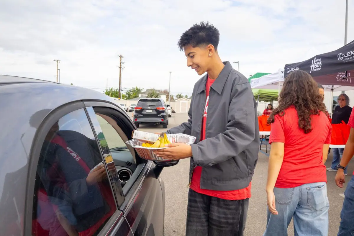 A volunteer offers a meal kit to an attendee, greeting him with a warm smile