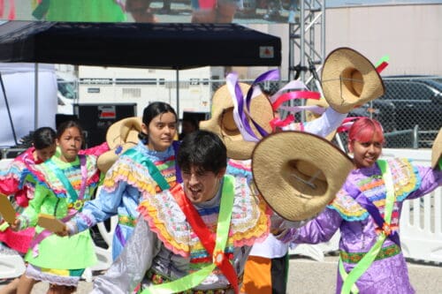 5 Peruvian dancers in colorful costumers wave straw hats.