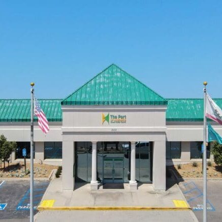 A building with a green roof labeled “The Port” stands proudly, its two flagpoles and accessible parking out front reflecting the $3.935 Million State Grant for Port of Hueneme as California ramps up its Port Data Partnership Program.