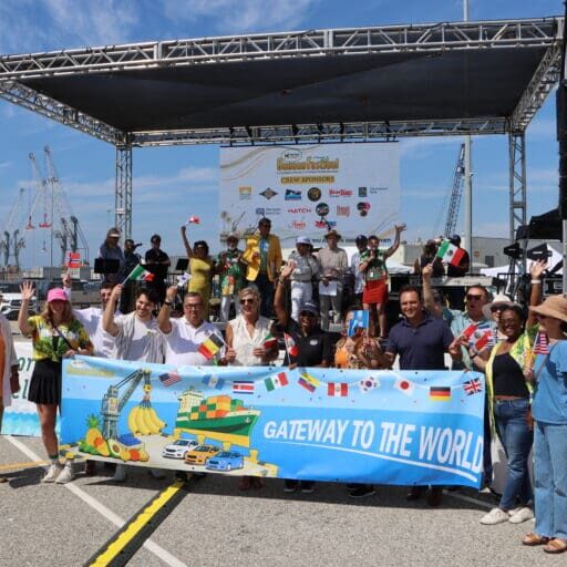 A group of people hold a small international flags and hold a banner with text reading GATEWAY TO THE WORLD.